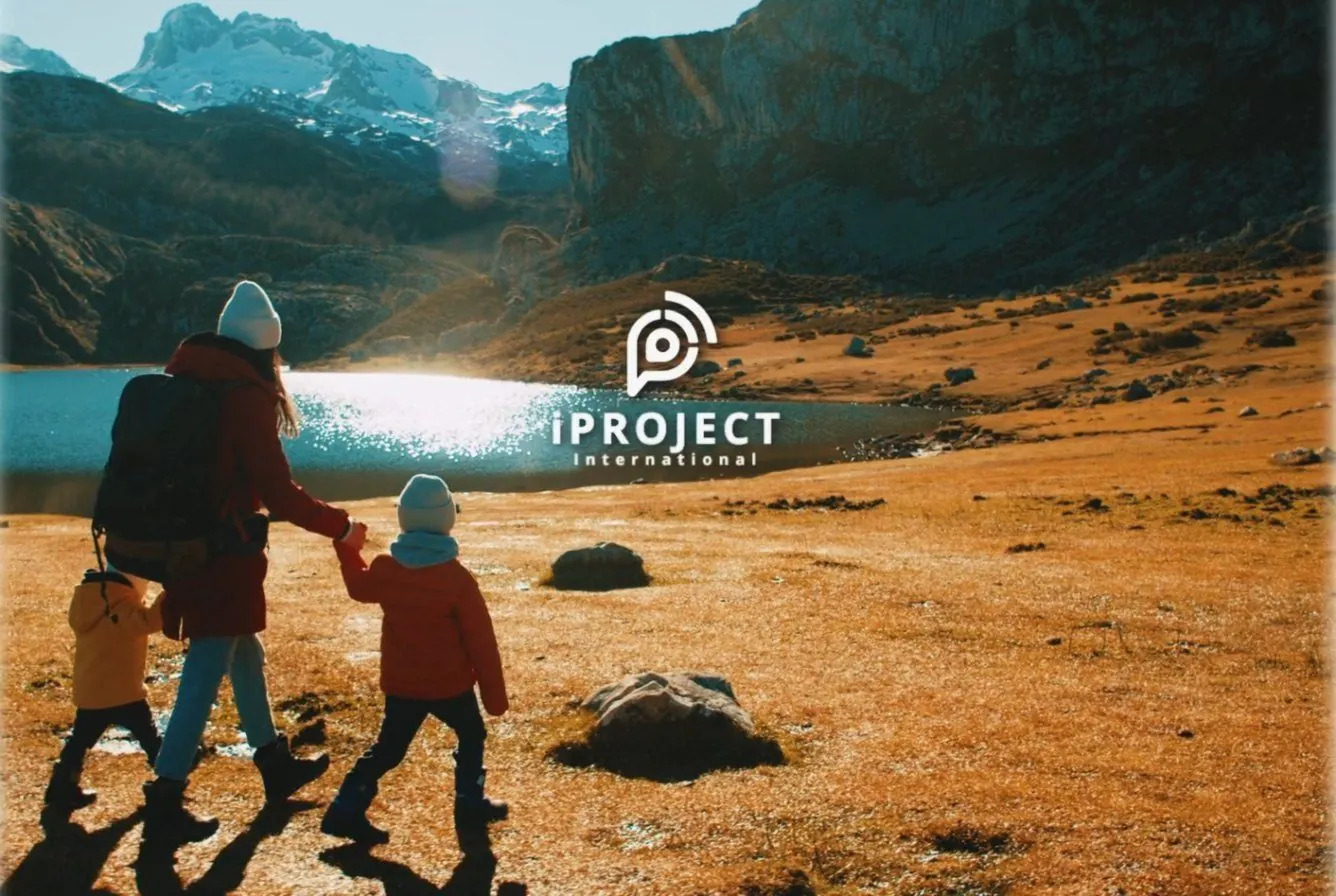 A parent and two children walking toward a mountain lake